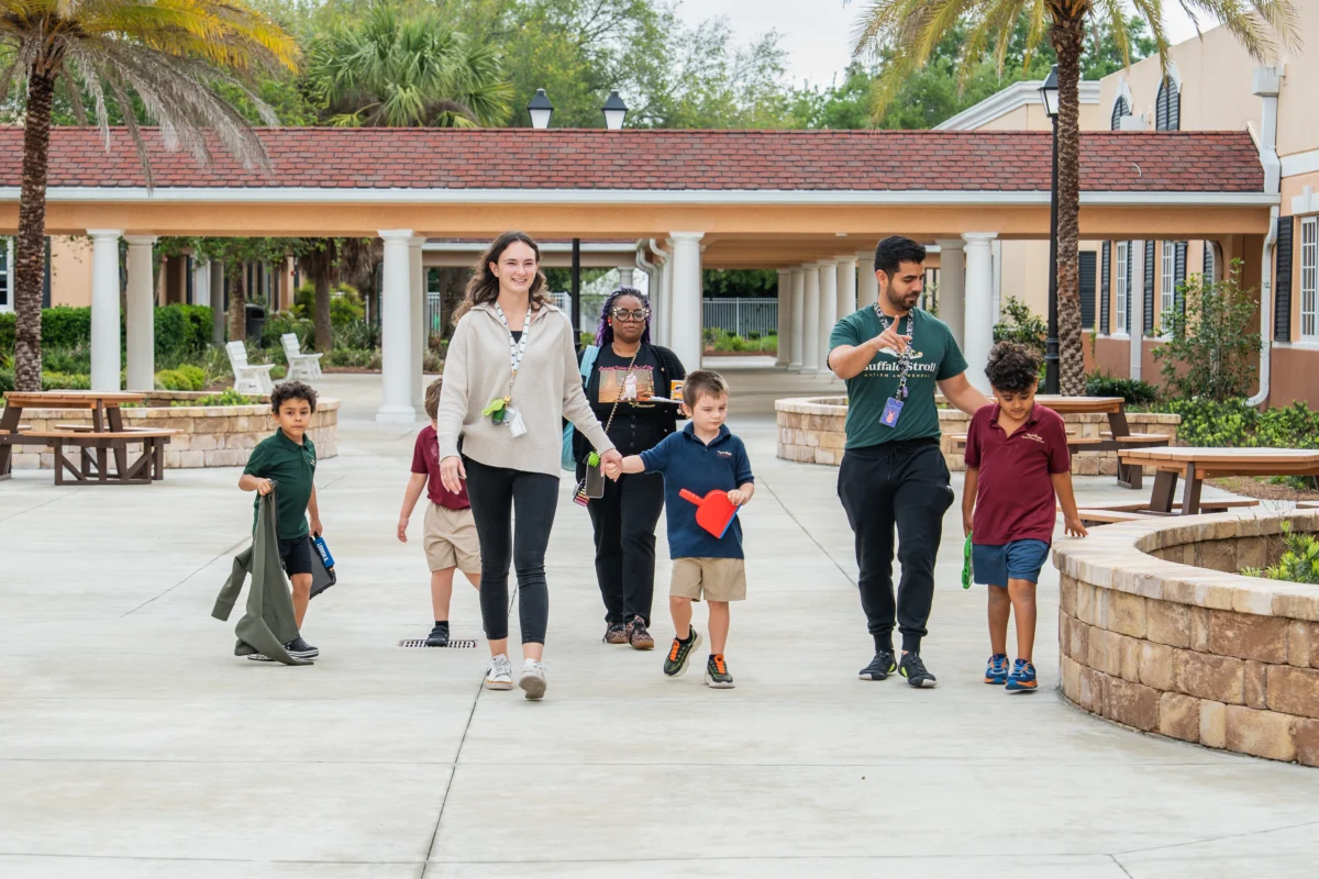Teachers happily escorting students across the courtyard of The Villages Charter School Autism Center